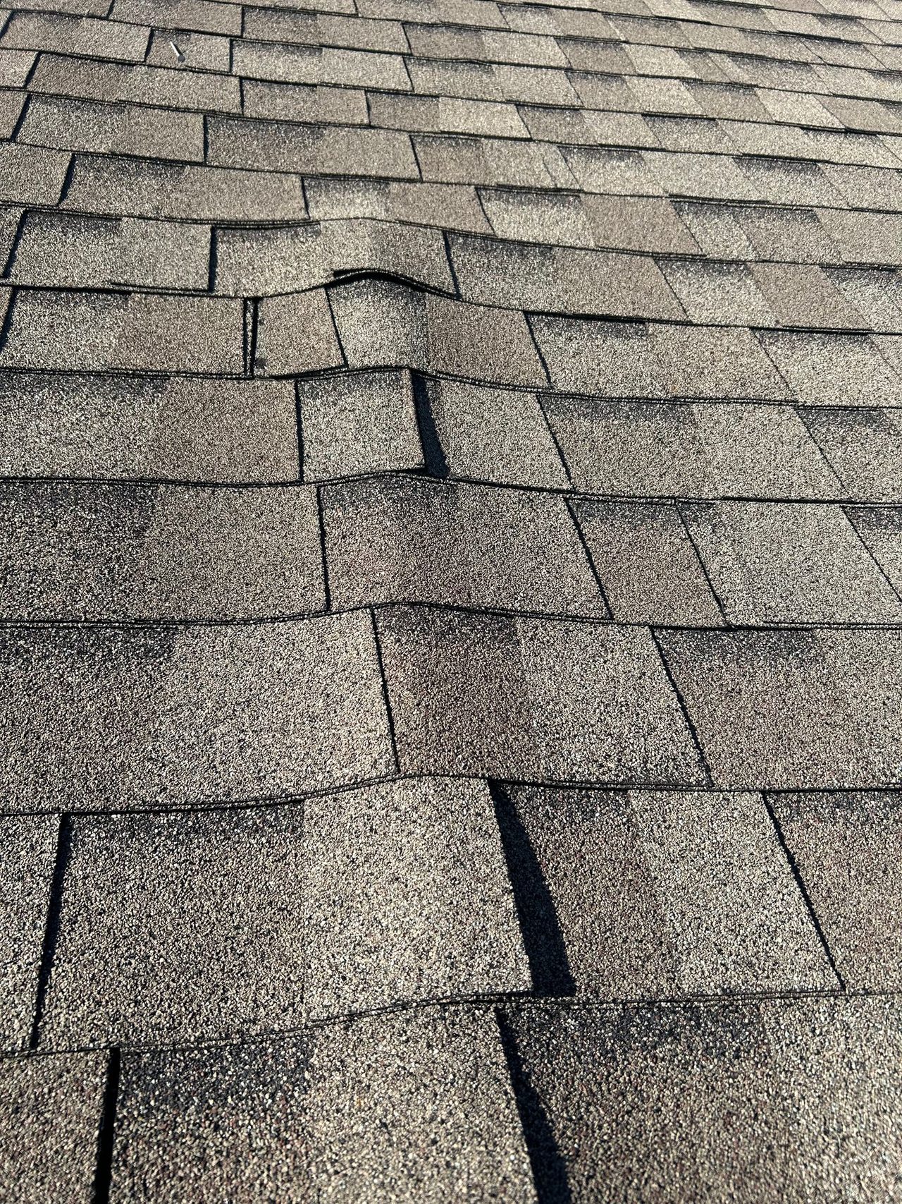 Close-up of wind-lifted, buckled shingles from storm damage