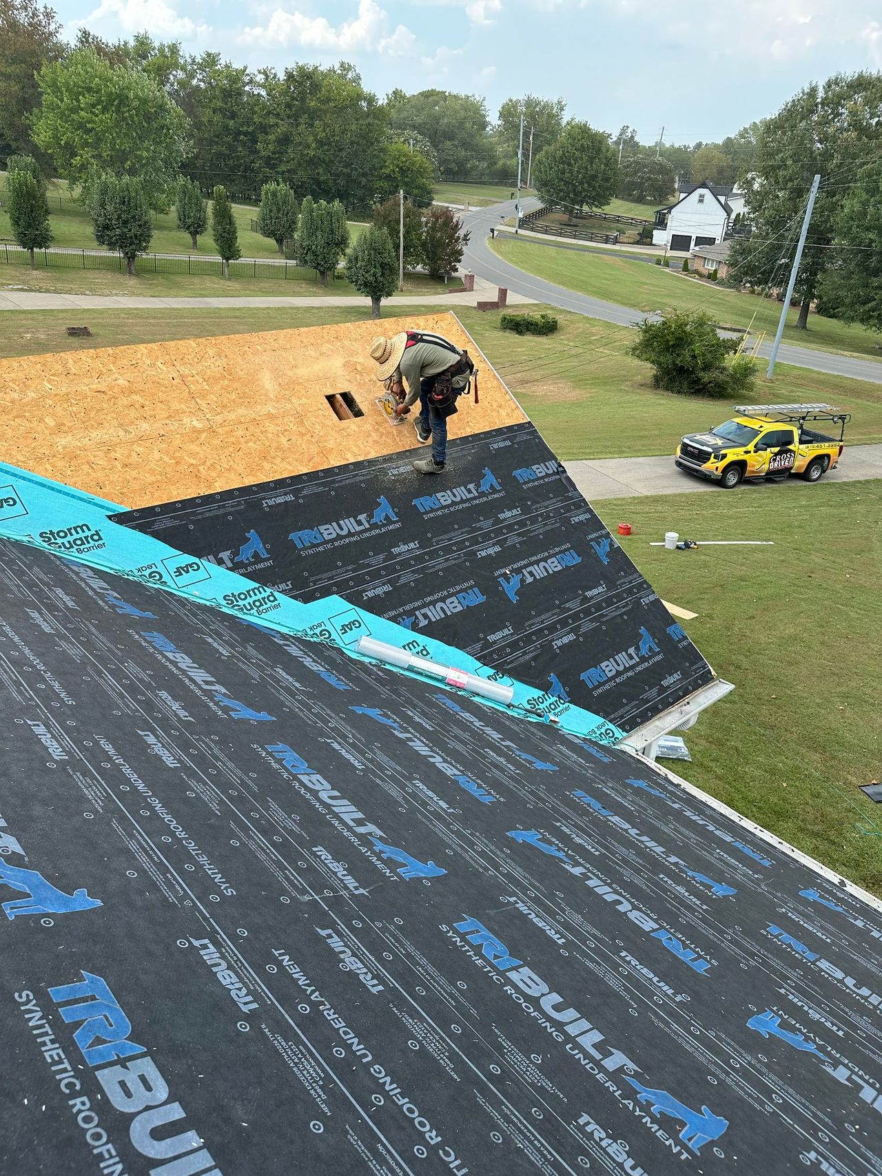 Crew installing synthetic underlayment on a roof deck, aerial view with a Cross Driven truck in the driveway