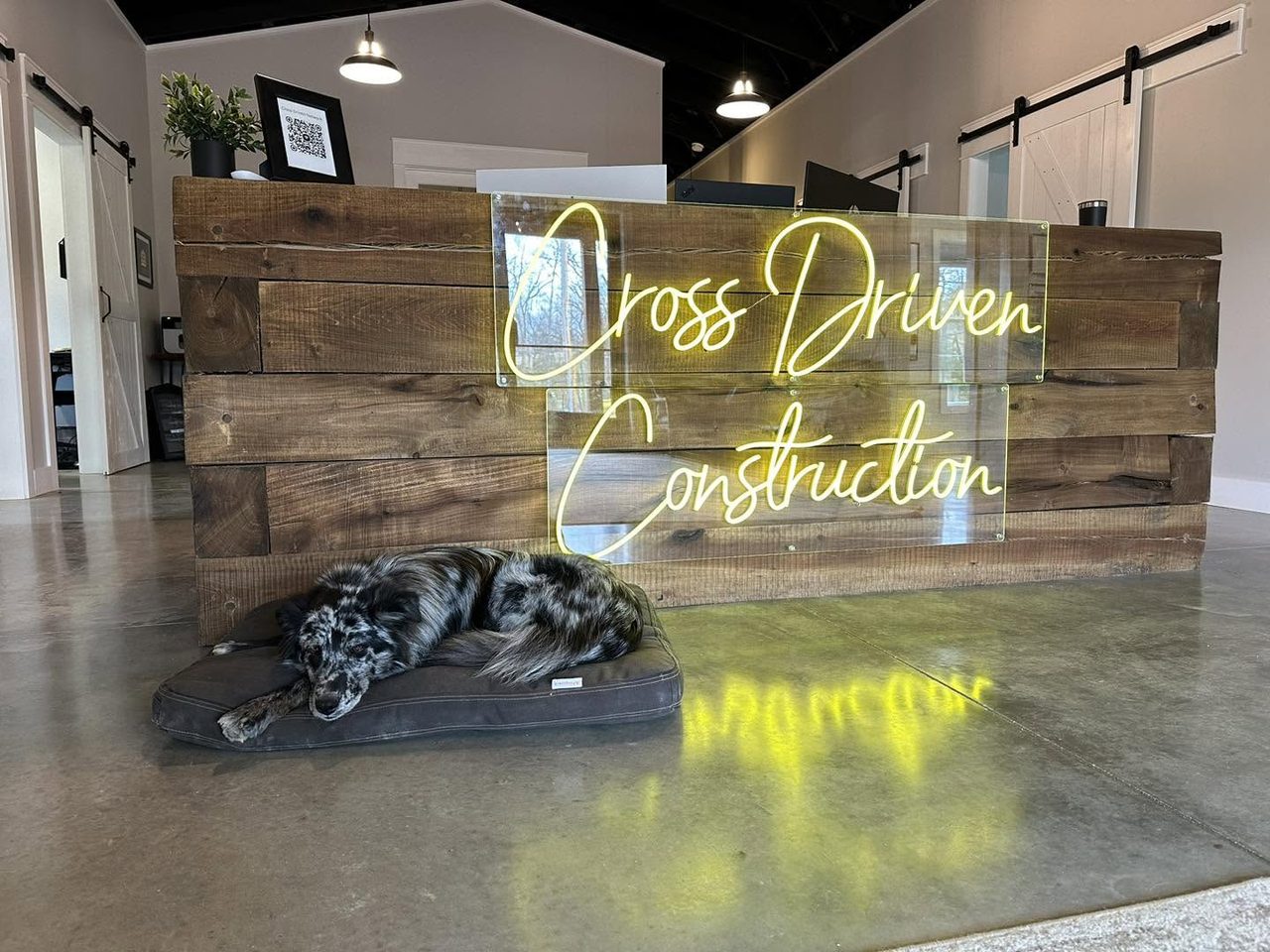 The Cross Driven Construction office: a reclaimed-wood reception desk with a neon company sign, and the office dog asleep in front of it
